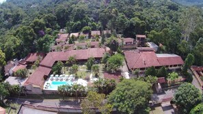 An aerial view of a resort with multiple buildings, a swimming pool, and lush greenery. - Hotel Fazendinha (Itatiaia)
