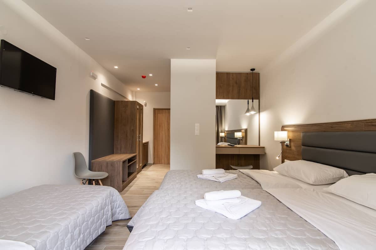 A modern hotel room with two beds, a desk, a chair, a TV, and a mirror.