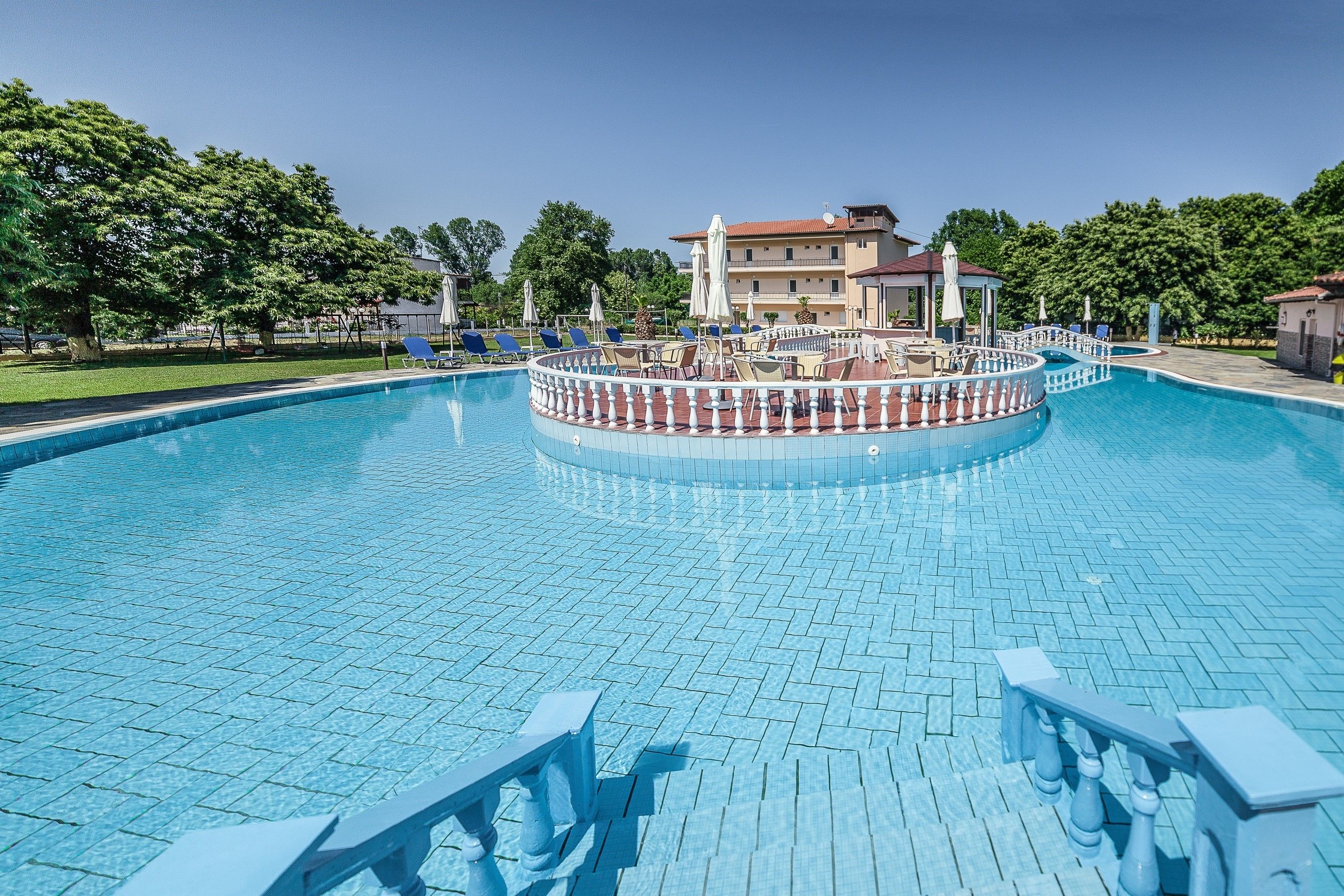 A large, circular swimming pool with a tiled deck and lounge chairs.