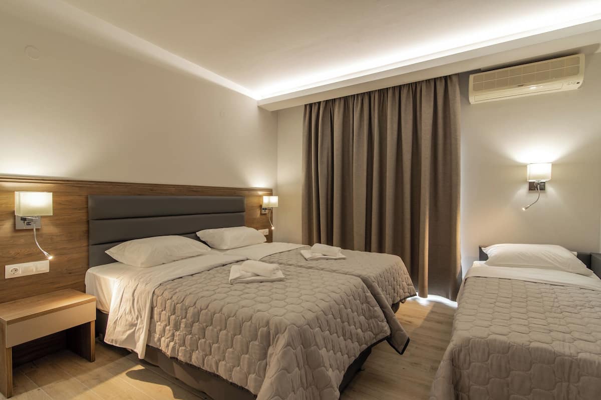 A hotel room with two beds, a bedside table, a nightstand, and a wall-mounted air conditioner.
