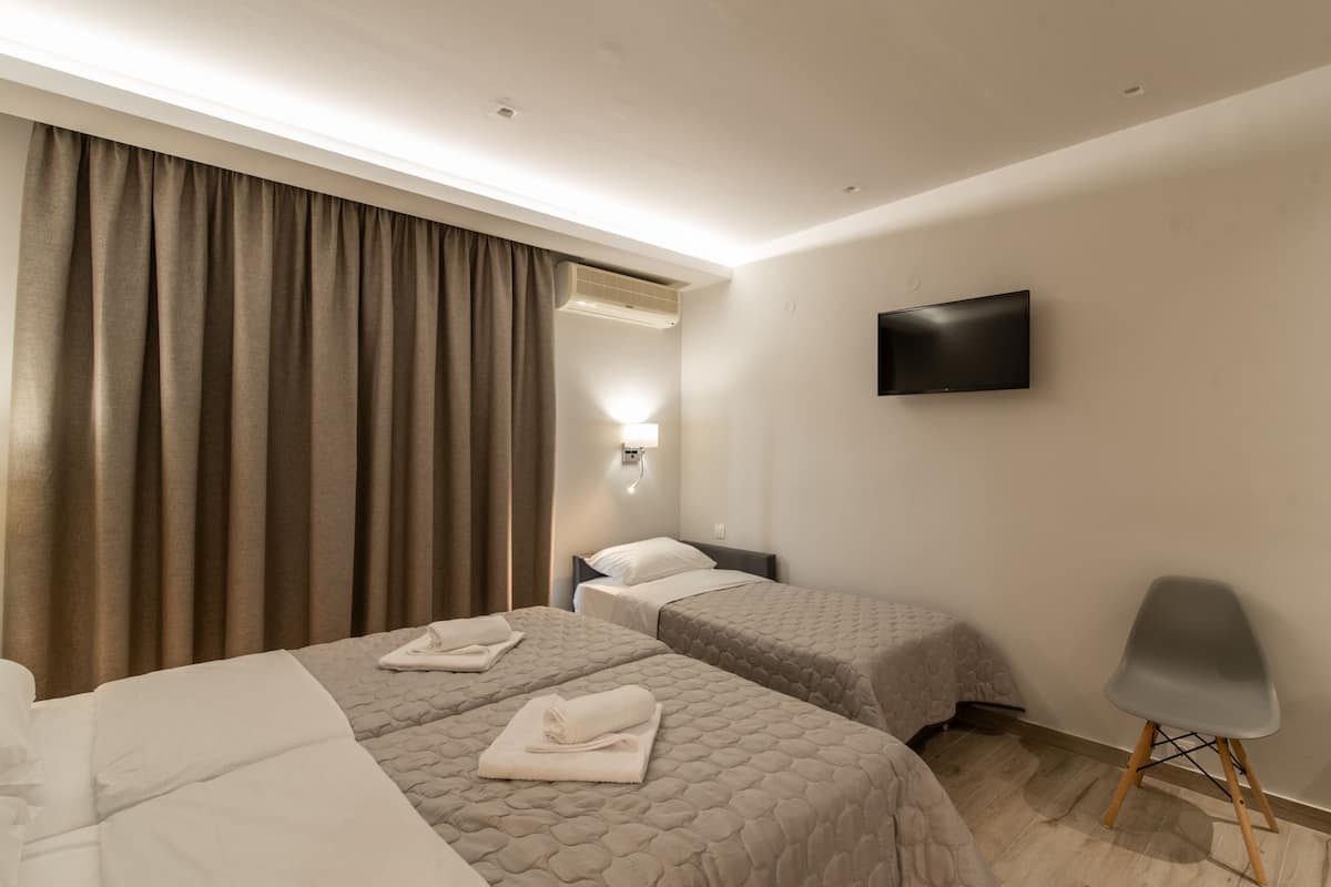 A hotel room with two beds, a flat-screen TV, a chair, and a window with curtains.