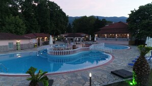 Una piscina con solárium de piedra, rodeada de sillones y sombrillas, con edificios al fondo.