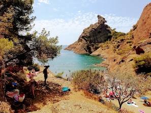 Une zone côtière caractérisée par un terrain rocheux, une mer bleue et limpide, et des personnes pratiquant diverses activités sur la plage.