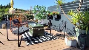 Een terras met buitenmeubilair, plantenbakken en een gebouw op de achtergrond.