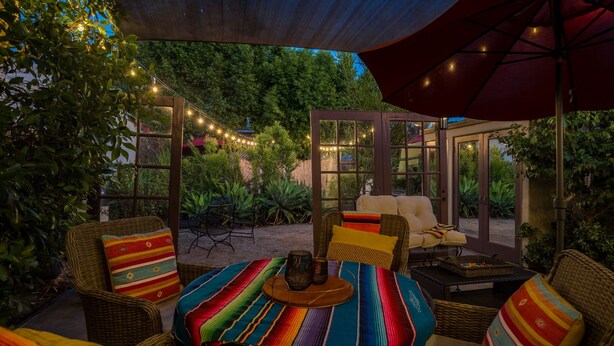 Eine Terrasse im Freien mit Korbmöbeln, einer bunten, gestreiften Tischdecke und Lichterketten.