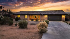 Une maison de plain-pied avec un toit en tuiles, un porche à l’avant et une allée menant à un garage.