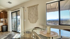 Une cuisine moderne avec une porte vitrée donnant sur un balcon, une décoration murale en macramé et un coin repas avec une table et des chaises en verre.