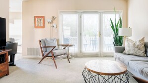 Una sala de estar con un sofá, una mesa de centro de madera, una silla, un televisor y una planta grande.
