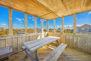 A wooden deck with a bench and a table, large windows, and a view of houses. - Oceanview Home with Private Pool, Hot Tub, Game Room, and Screened Porch (Salvo)