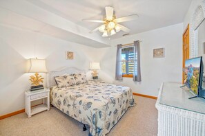 A bedroom with a bed, two bedside tables with lamps, a ceiling fan, a window with curtains, a wall clock, and a television. - Oceanview Home with Private Pool, Hot Tub, Game Room, and Screened Porch (Salvo)