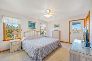 A bedroom with a bed, a dresser, a nightstand, a ceiling fan, and a view of a house through a door. - Oceanview Home with Private Pool, Hot Tub, Game Room, and Screened Porch (Salvo)