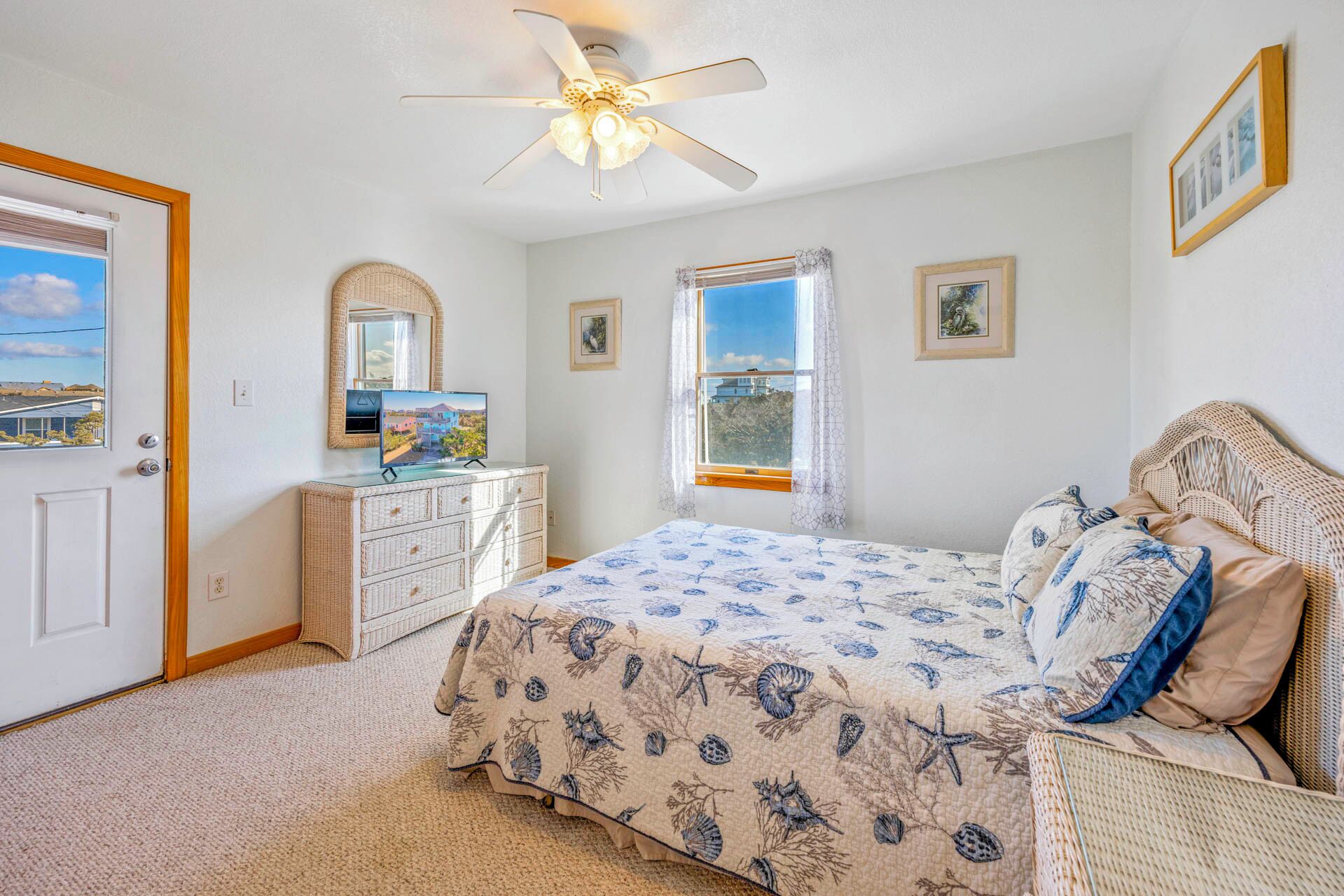 A bedroom with a bed, dresser, ceiling fan, and a window with curtains.