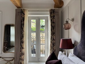 A room with a bed, a nightstand, a lamp, a mirror, and a door leading to an outdoor area with a view of greenery. - Manor House Lindley (Huddersfield)