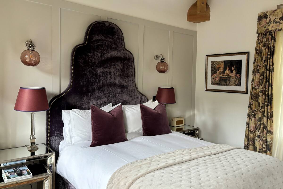 A hotel room with a large bed, two bedside lamps, a framed picture on the wall, and a window with curtains.