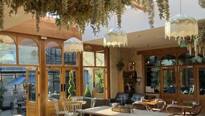 A restaurant with wooden tables and chairs, hanging plants, and large windows. - Manor House Lindley (Huddersfield)