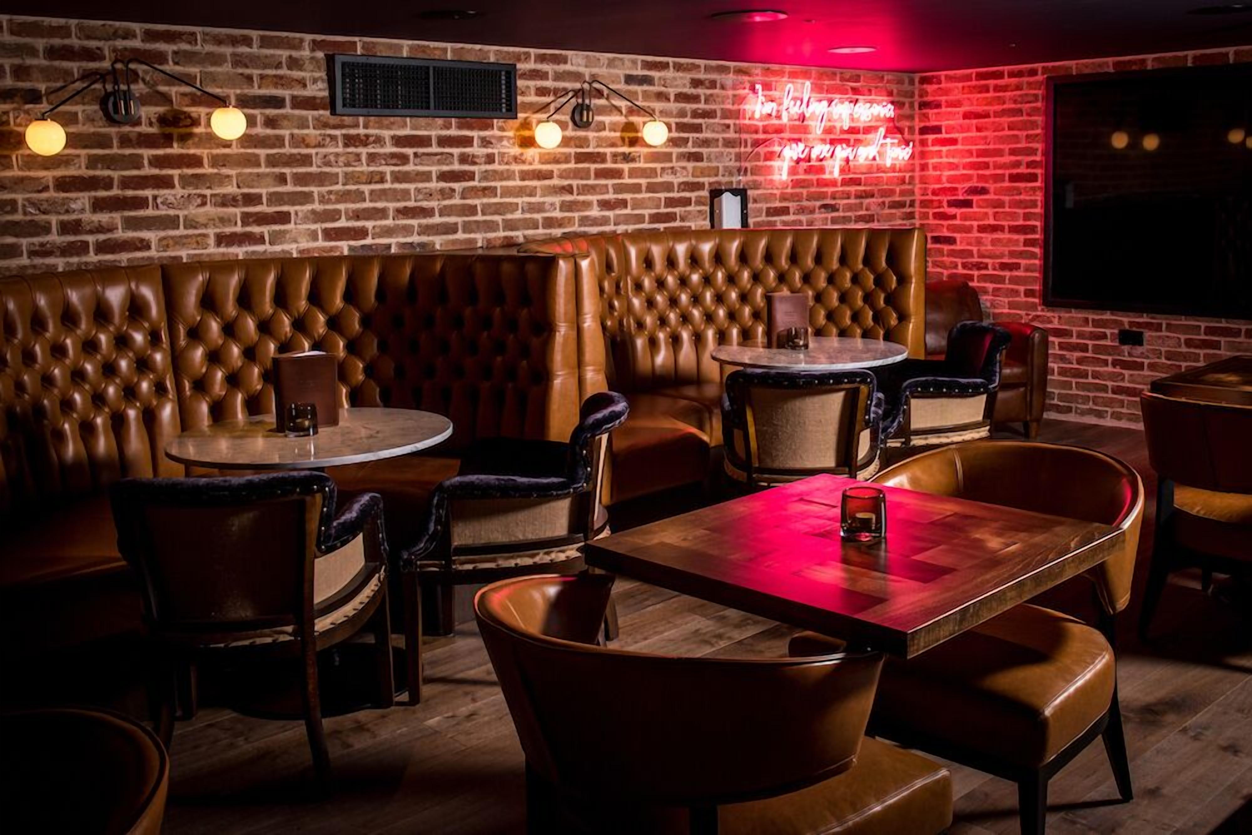 A cozy restaurant with leather booths and wooden tables, brick walls, and a neon sign.
