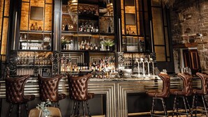 A bar area with a stone wall backdrop, multiple shelves of liquor bottles, and leather bar stools. - Manor House Lindley (Huddersfield)