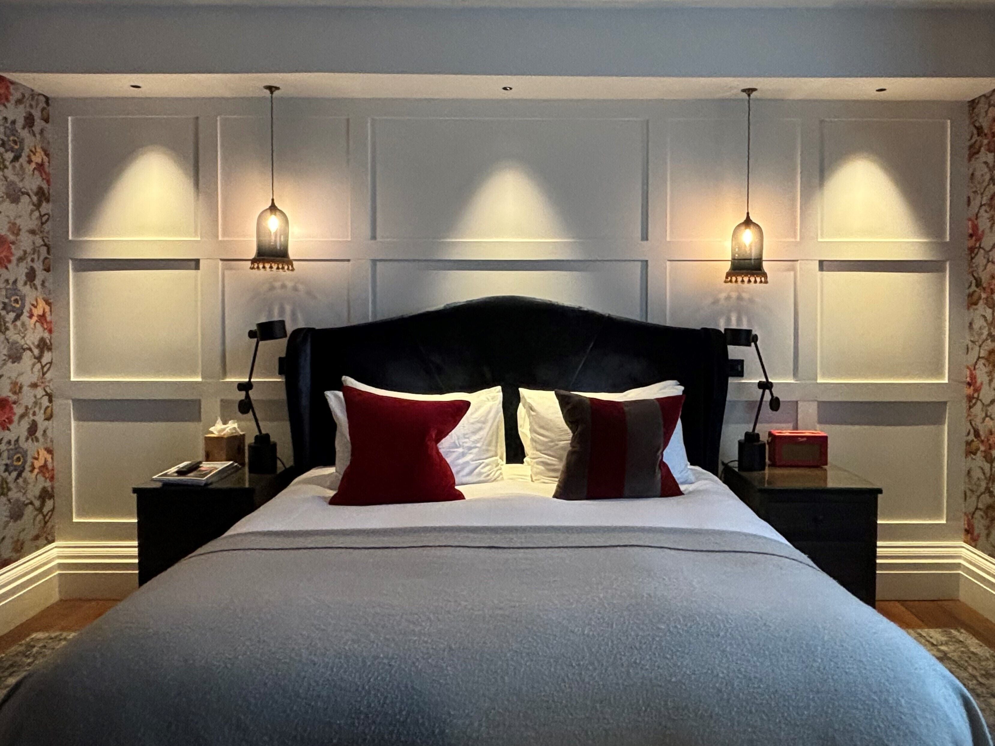 A neatly made bed with a dark headboard, two bedside tables with lamps, and floral wallpaper on the walls.