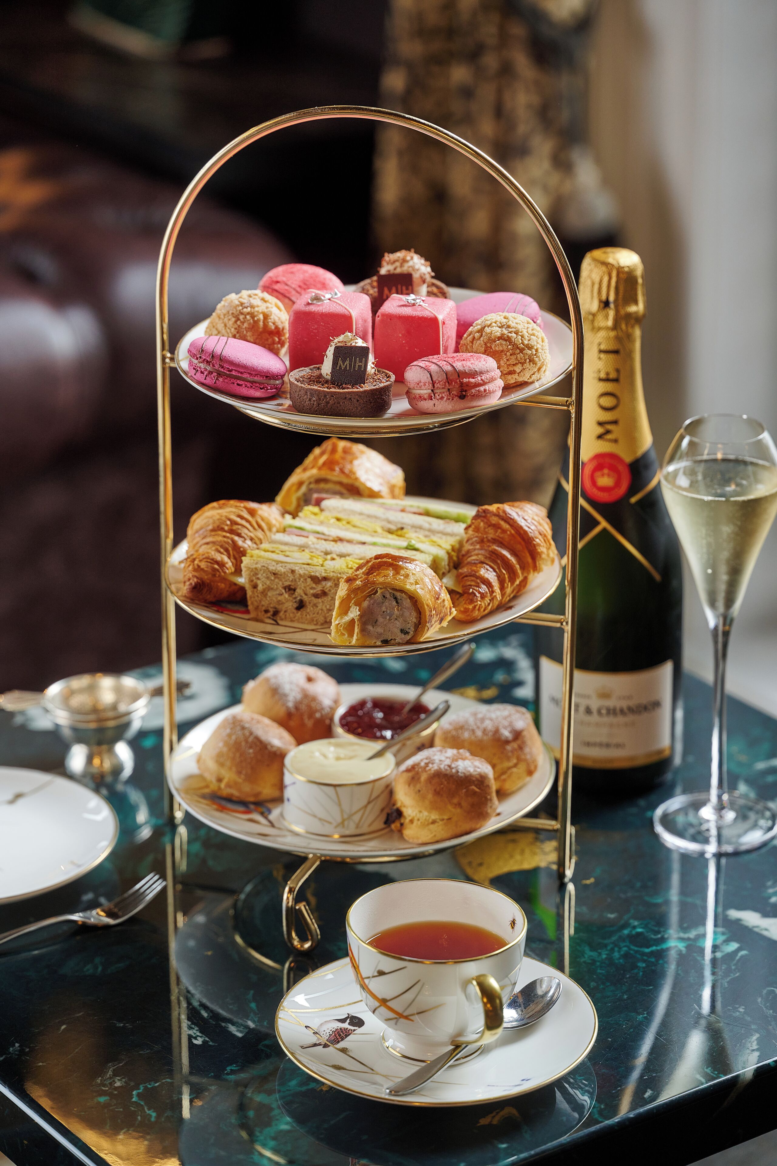 A tiered dessert stand with pastries and a bottle of champagne on a table.