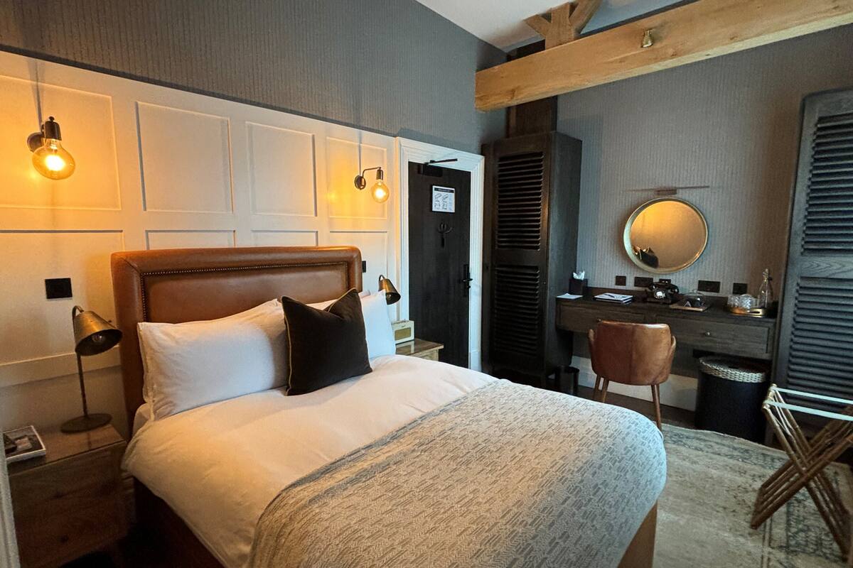 A hotel room with a bed, bedside lamp, dresser, mirror, and a chair.