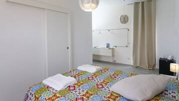 Un dormitorio con cama, mesita de noche, lámpara colgante, baño con espejo y cortina de ducha.