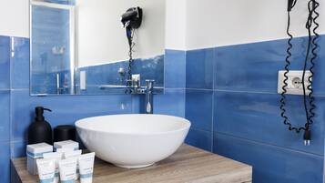 A bathroom with a white sink, blue tiles, a wooden vanity, and a hairdryer mounted on the wall.