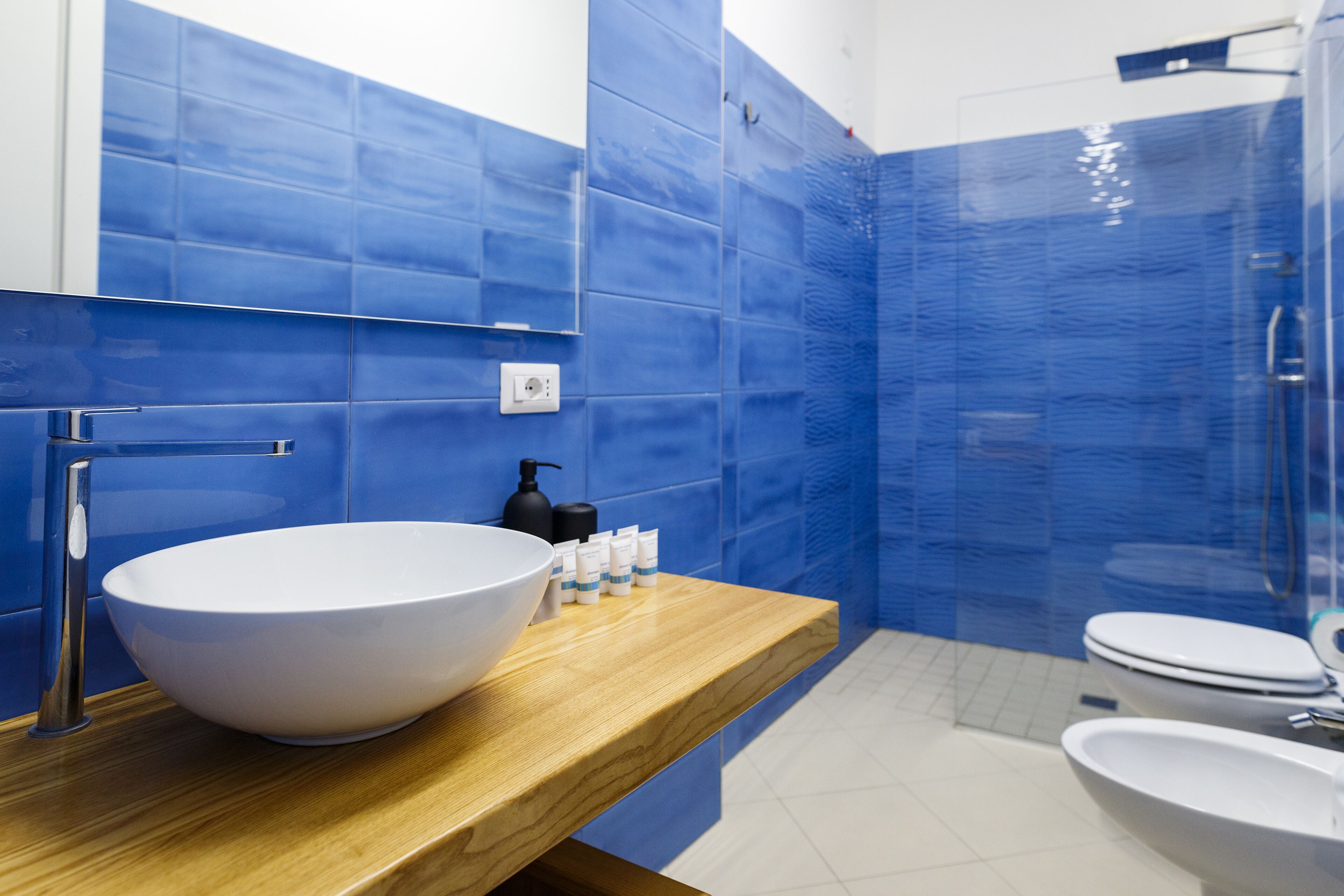 Un baño moderno con un lavabo blanco tipo cuenco, encimera de madera y paredes de azulejos azules.