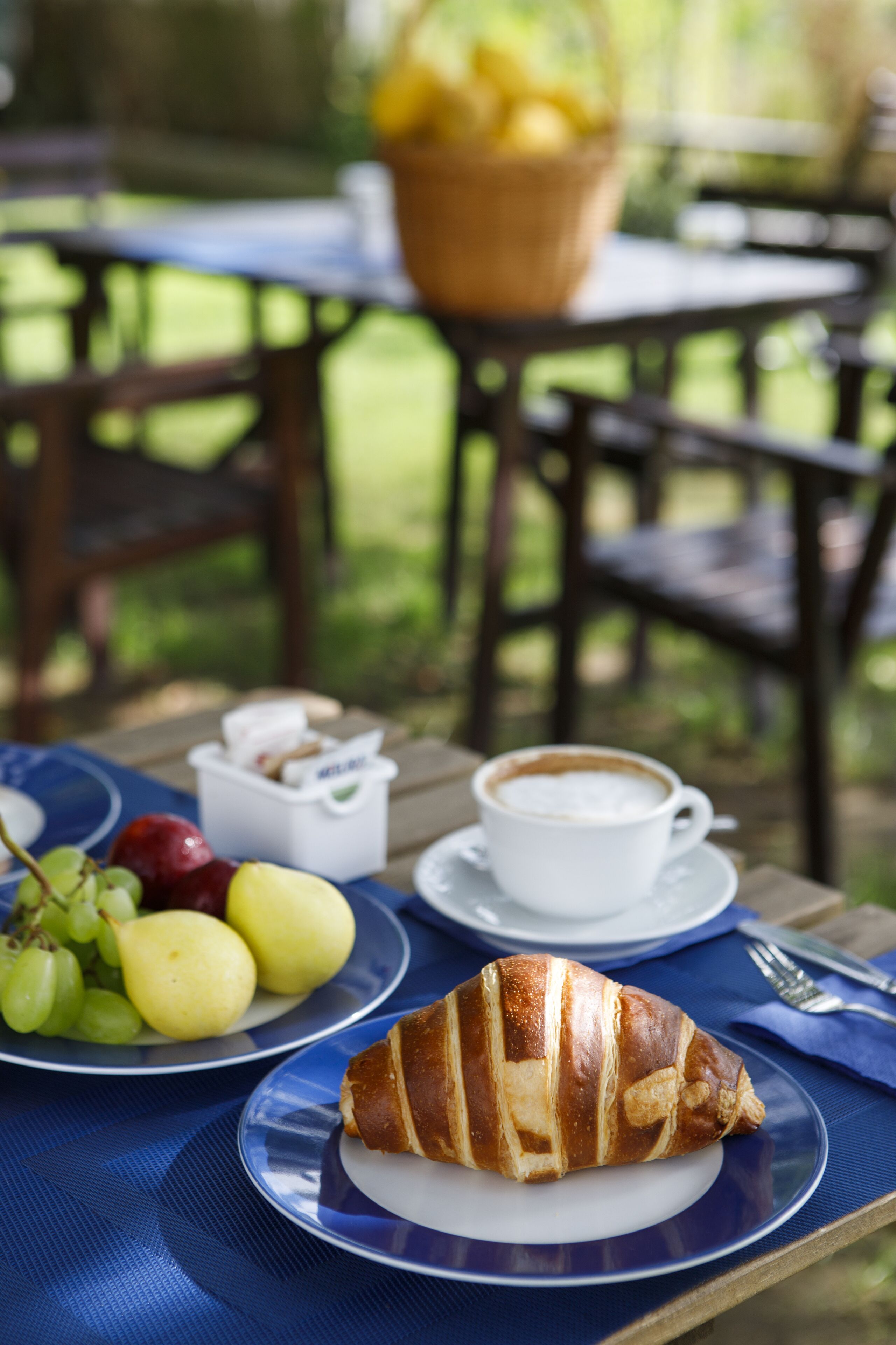A table with a croissant, a cup of coffee, and plates of fruit.
