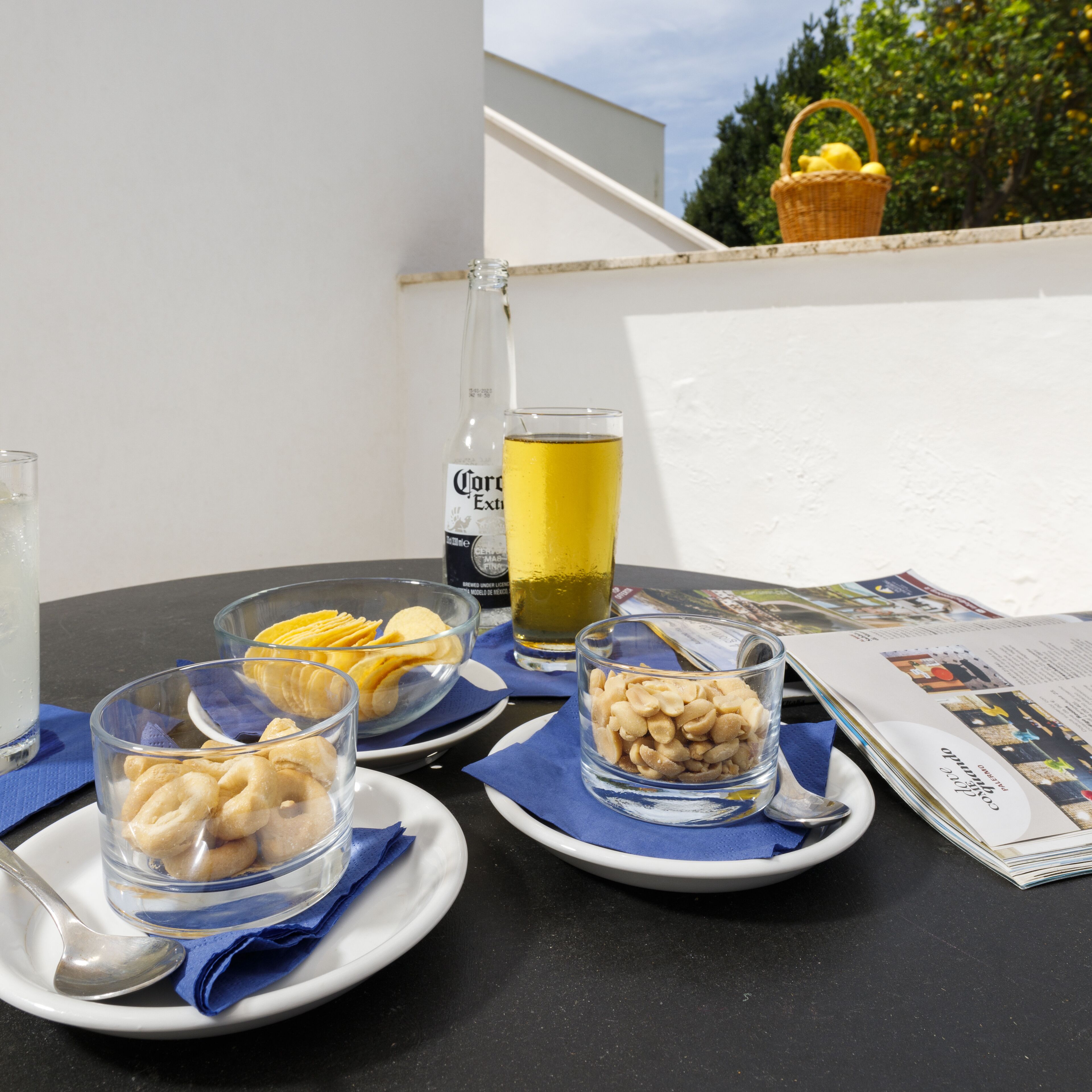 A table with plates of snacks, a bottle of beer, and glasses of beer and lemonade.