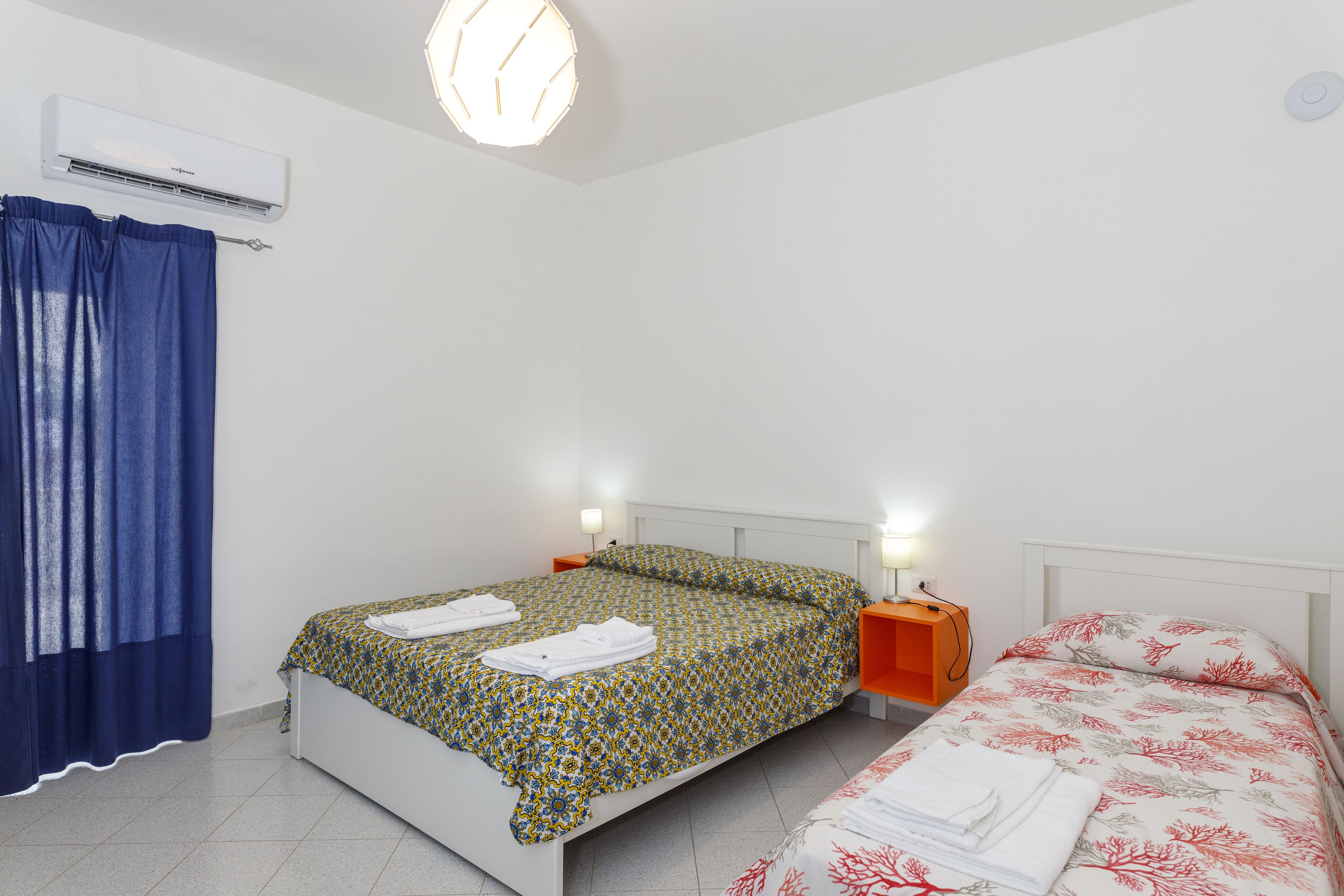 Une chambre à coucher avec un lit, une table de chevet, un climatiseur et une fenêtre avec des rideaux.