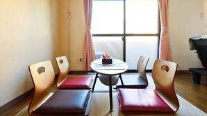 Una habitación con una mesa redonda, cuatro sillas, una mesita con un objeto rojo y una parrilla.
