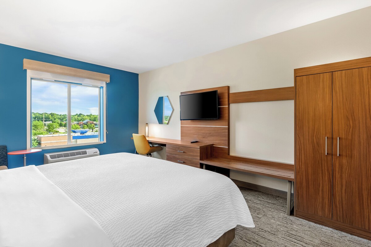 A hotel room with a bed, a desk, a chair, a TV, and a wardrobe.