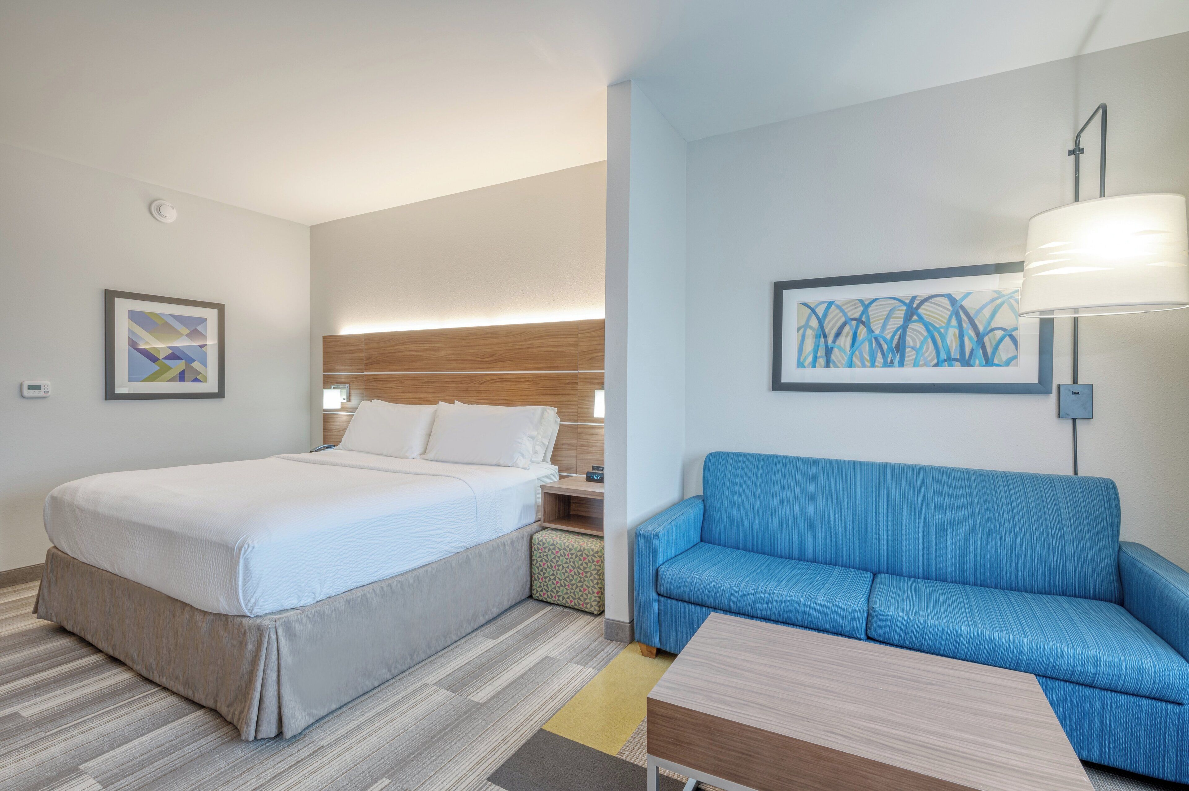 A hotel room with a bed, a blue sofa, a small table, and a lamp.