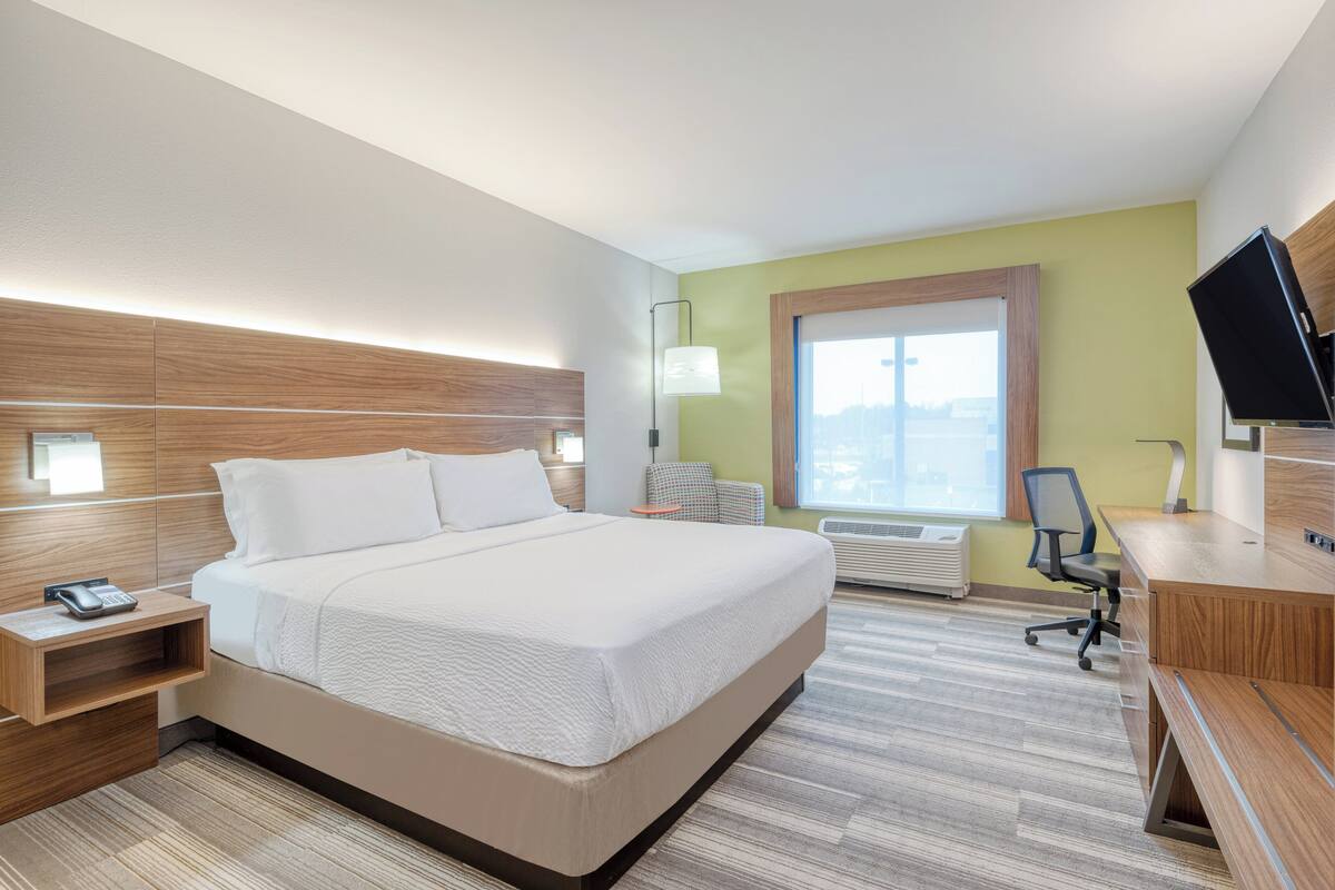 A hotel room with a large bed, bedside tables, a desk, a chair, a TV, and a window with a view.