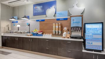 A breakfast bar with labeled sections for hot food, fruit, and cereal, and a yogurt dispenser.