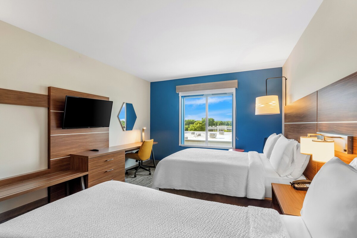 A hotel room with a bed, a desk with a chair, a television, and a window with a view of the outdoors.