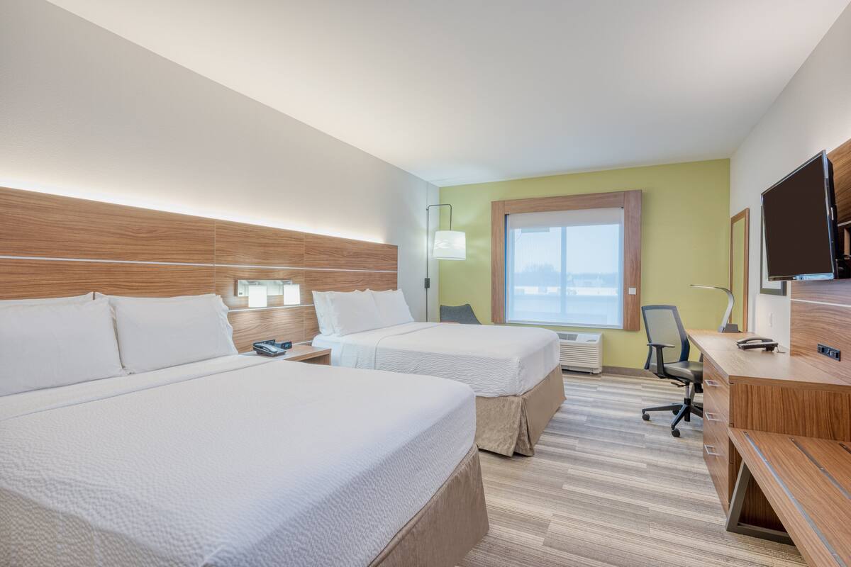 A hotel room with two beds, a desk, a chair, a TV, and a window.