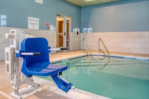 Ein Poolbereich mit blauem Poollifter, Schild zur Angabe der maximalen Nutzerzahl und einer gefliesten Wand.