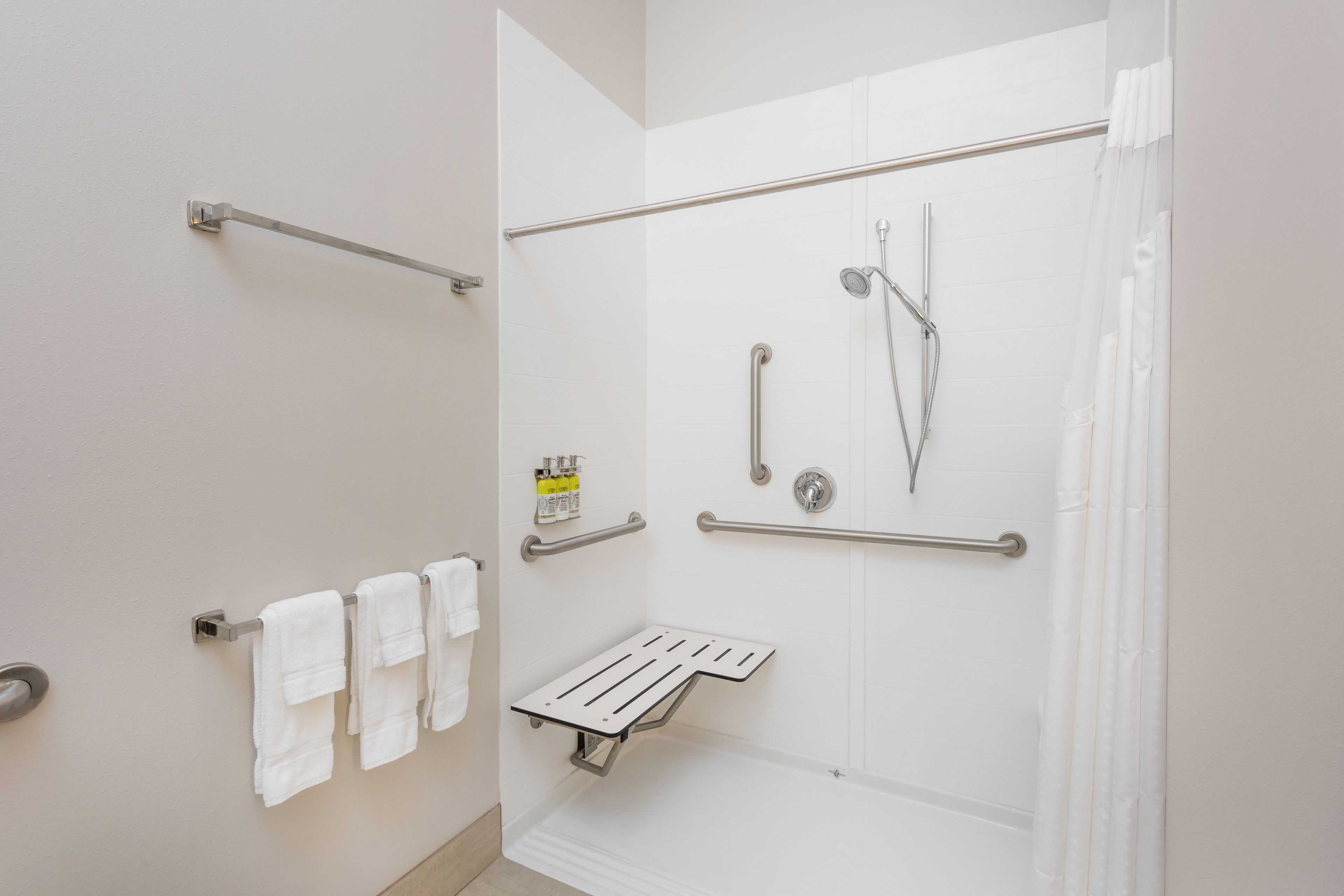 Een moderne badkamer met een inloopdouche, handgrepen, een handdoekhouder en een douchemanden.