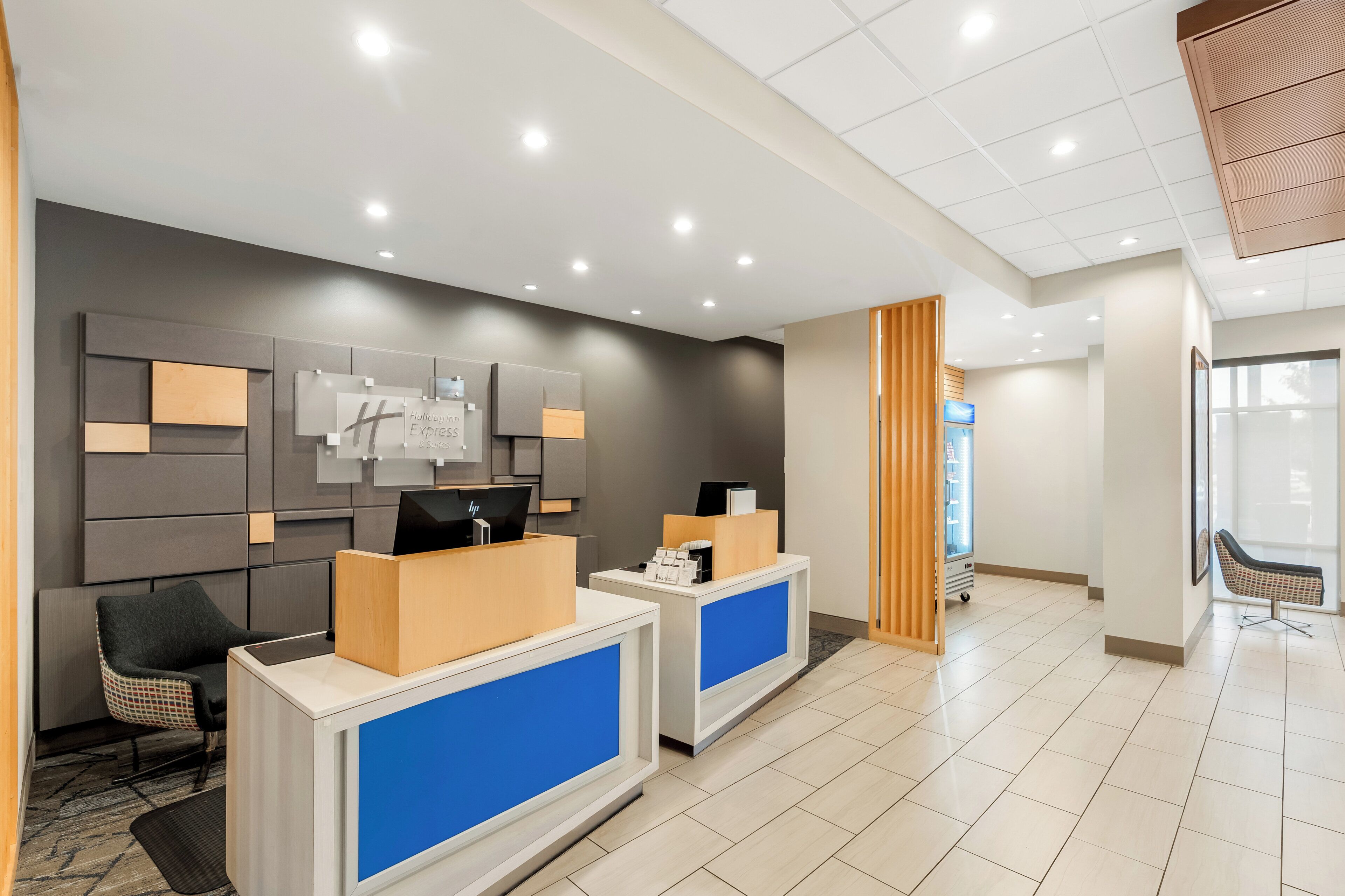 A hotel reception area with a modern design, featuring a reception desk, a seating area, and a wall-mounted information board.