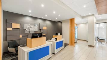 A hotel reception area with a modern design, featuring a reception desk, a seating area, and a wall-mounted information board.