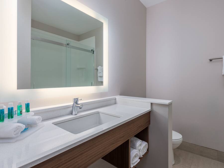 A modern bathroom with a large mirror, white sink, and wooden vanity.