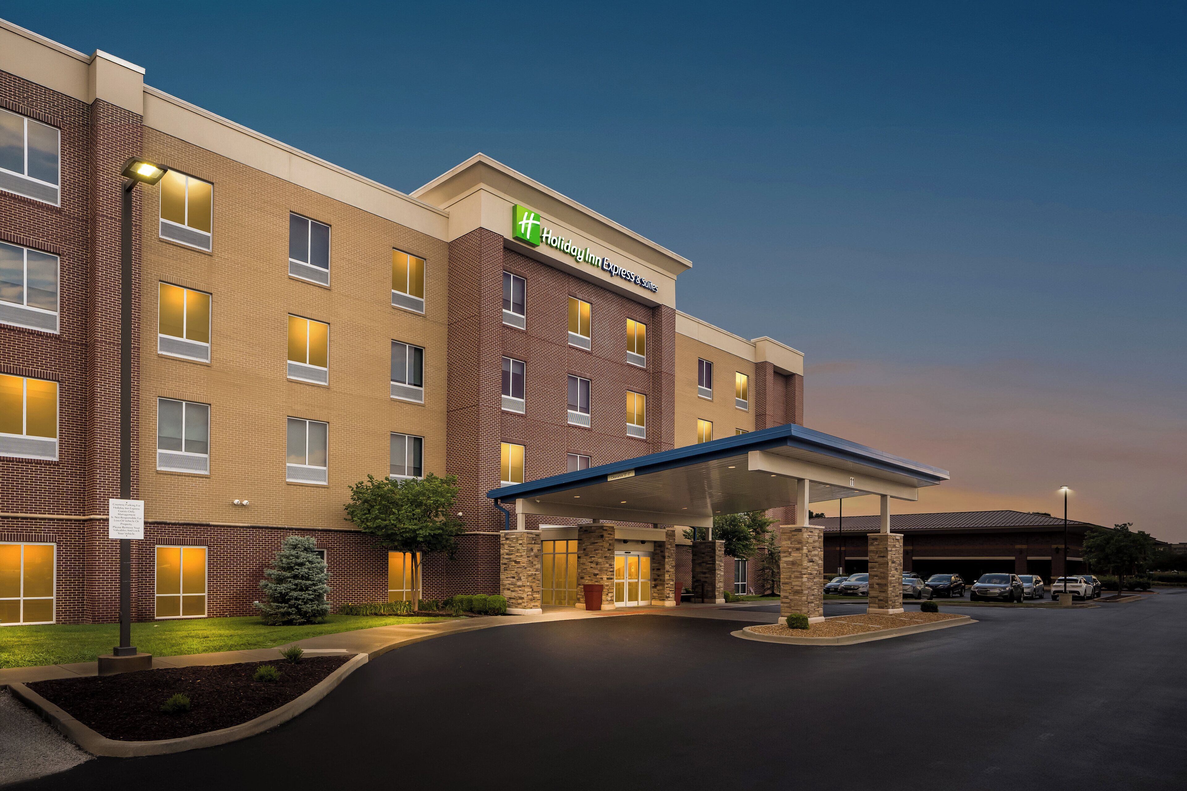 A Holiday Inn Express & Suites building with a covered entrance, parking area, and a brick facade.