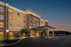 En byggnad som inrymmer ett Holiday Inn Express & Suites-hotell, med en ingång som är skyddad av ett tak, en parkeringsplats och en fasad av tegel.