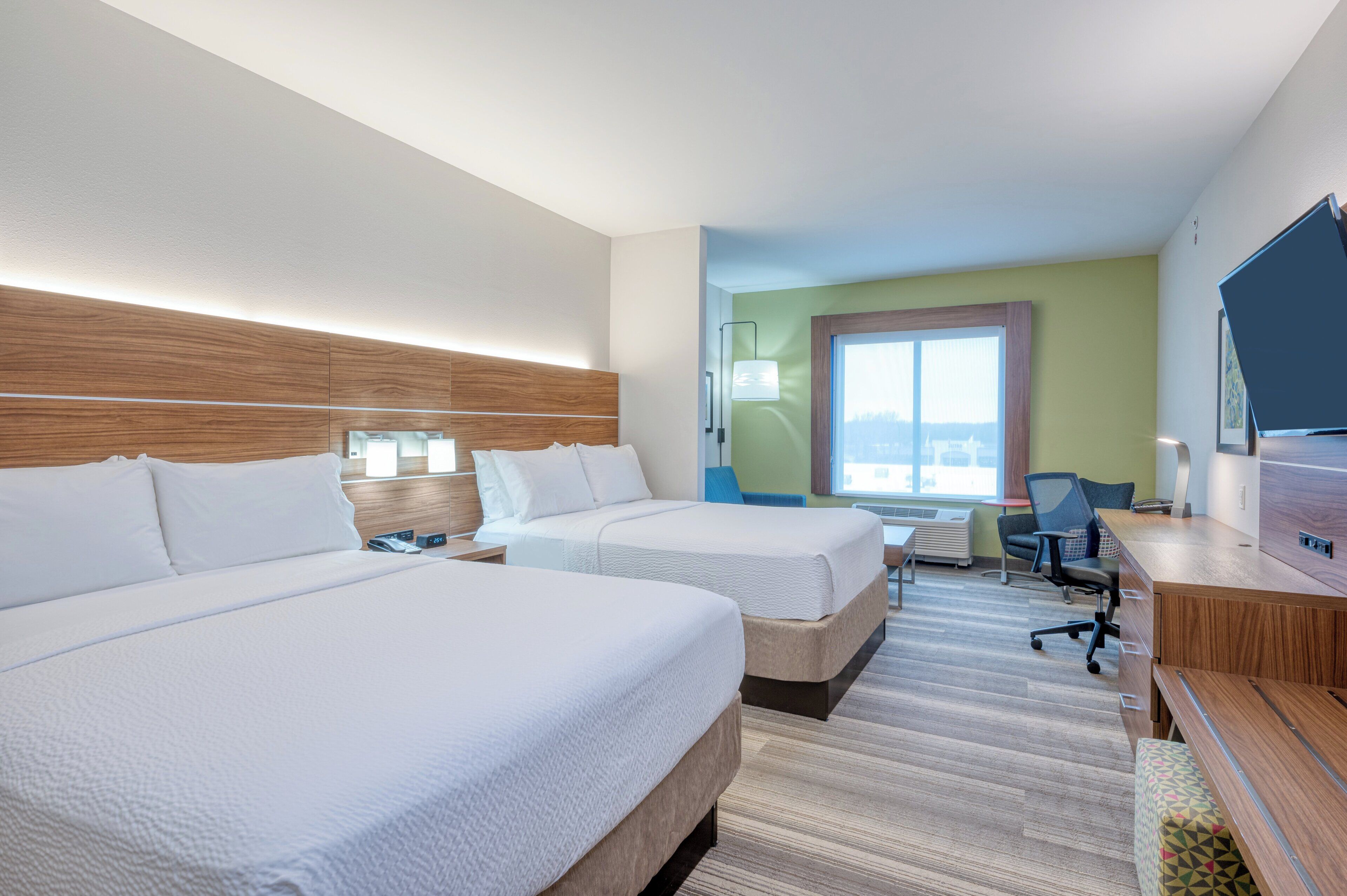 A hotel room with two beds, a desk, a chair, a television, and a window with a view.