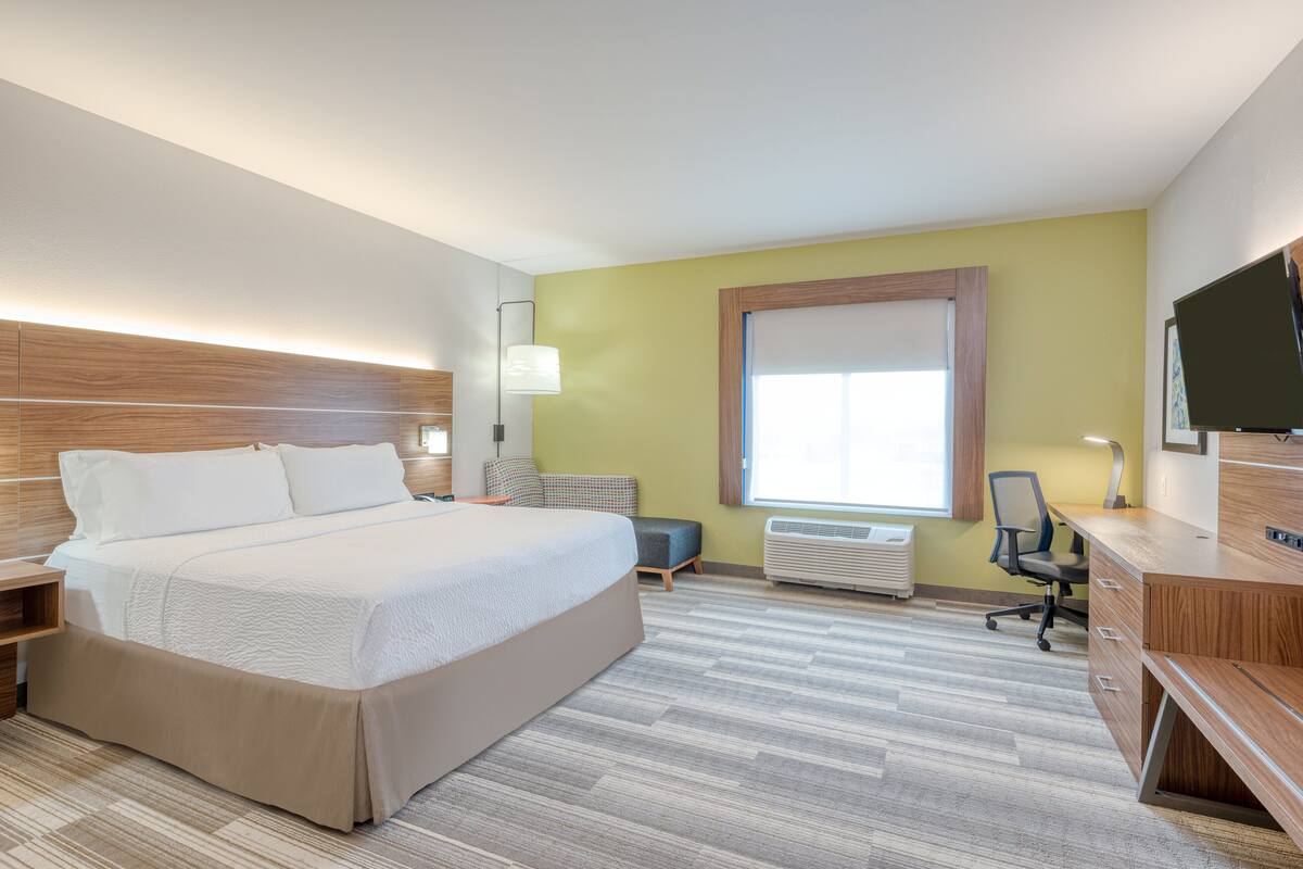 A hotel room with a bed, desk, chair, and a large window.