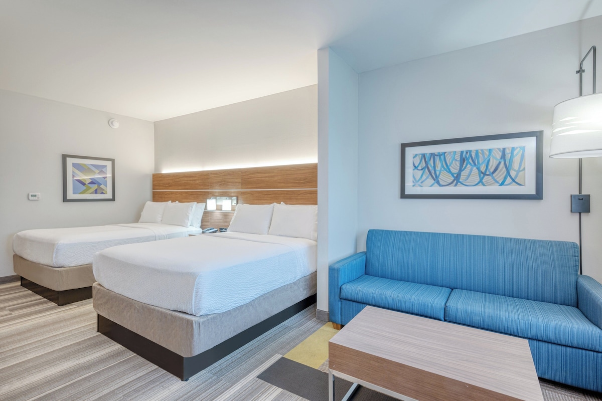 Ein Hotelzimmer mit zwei Betten, einem blauen Sofa, einer Lampe und abstrakter Kunst an den Wänden.