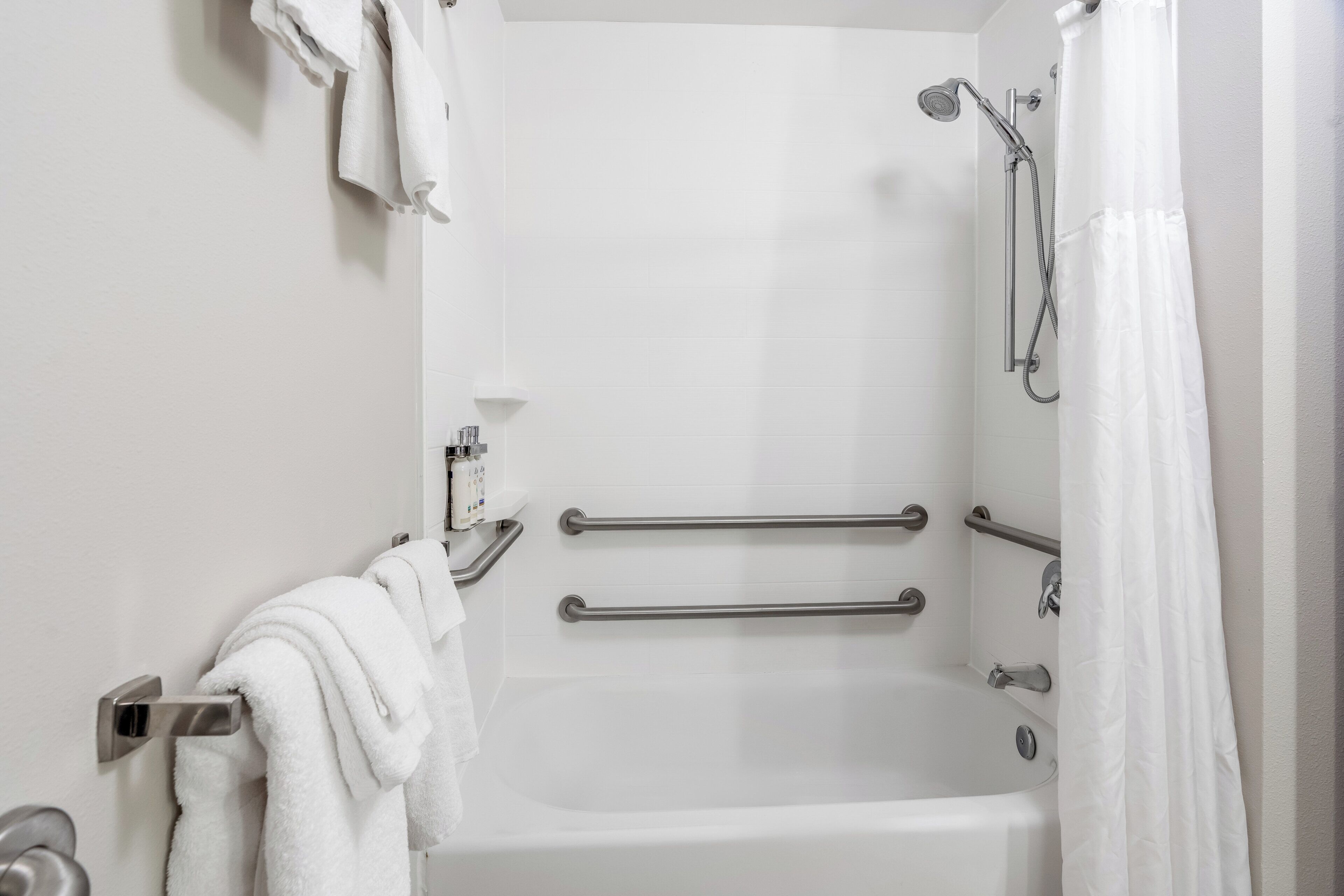 A bathroom with a white bathtub, grab bars, a showerhead, and a towel rack.