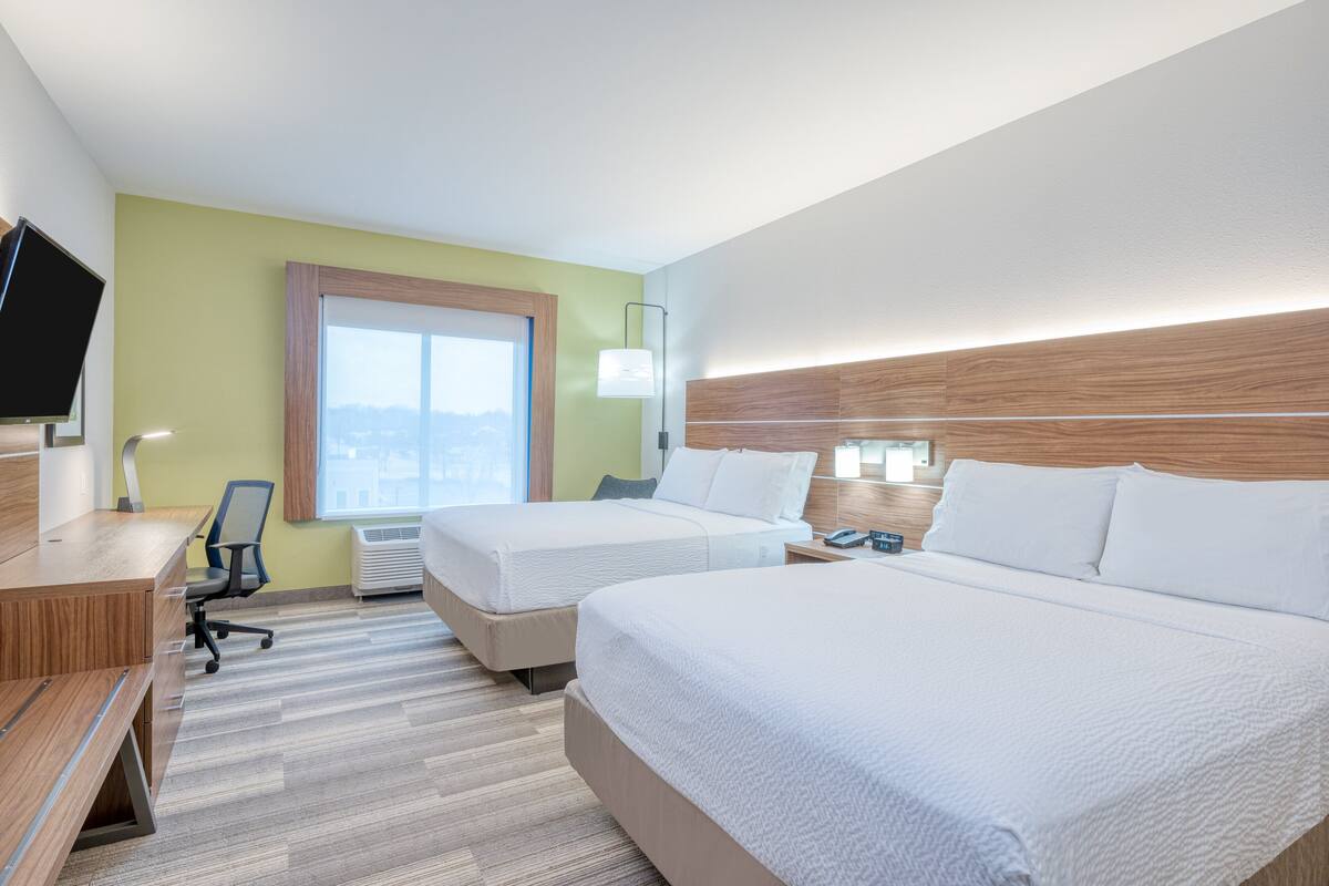 A hotel room with two beds, a desk, a chair, a TV, and a window with a view.