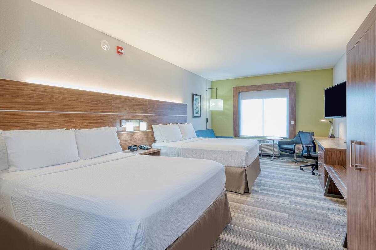 A hotel room with two beds, a desk, a chair, a TV, and a window.